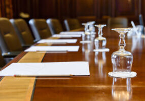 Large wooden table in a board room with wood panelling, set up for a meeting